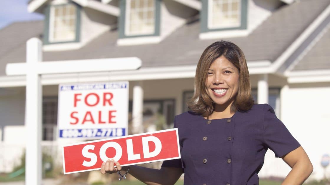 real estate agent holding a SOLD sign in front of a house