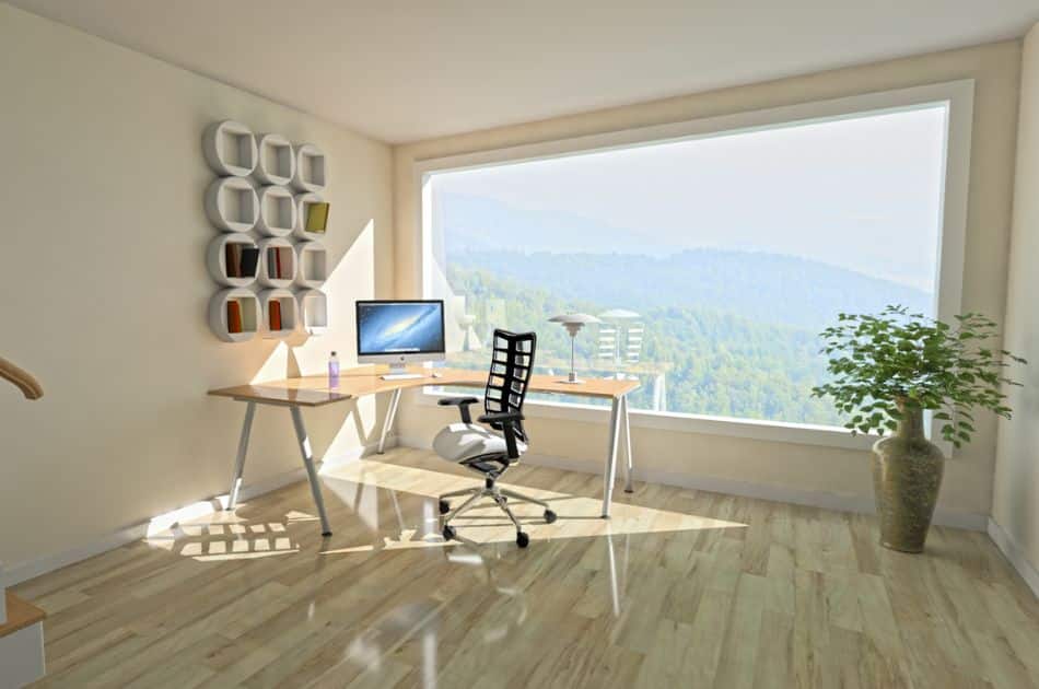 A home office with a computer and chair, featuring a large window for natural light and a view.