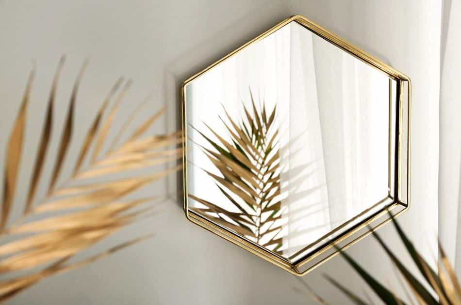 A gold mirror on a wall with a reflection of gold tropical leaves.