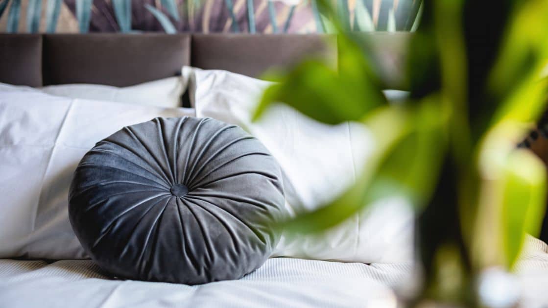 Close-up of a bed in a staged bedroom with a grey circle pillow on the bed.