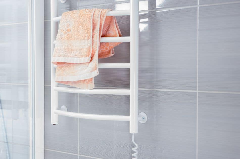 Empty bathroom with gray colored shower wall behind white metal towel warming rack with a pink folded towel on top.