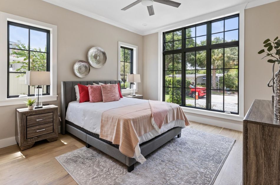 Bright bedroom with large black-trimmed windows, neutral decor, and red and pink accent pillows.