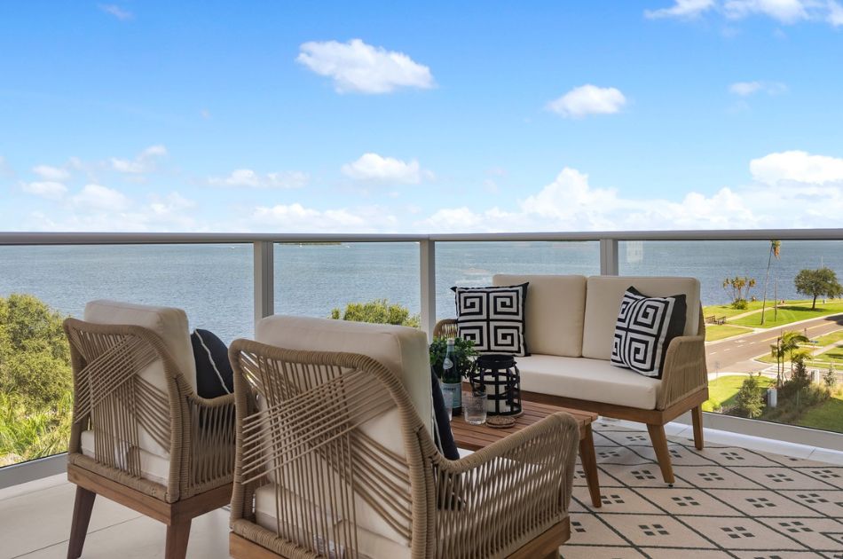 Outdoor balcony with woven chairs and a loveseat overlooking a waterfront view.