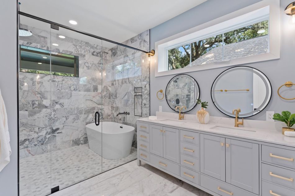 Bathroom with marble tile, a glass-enclosed shower, freestanding tub, and double vanity with gold fixtures.